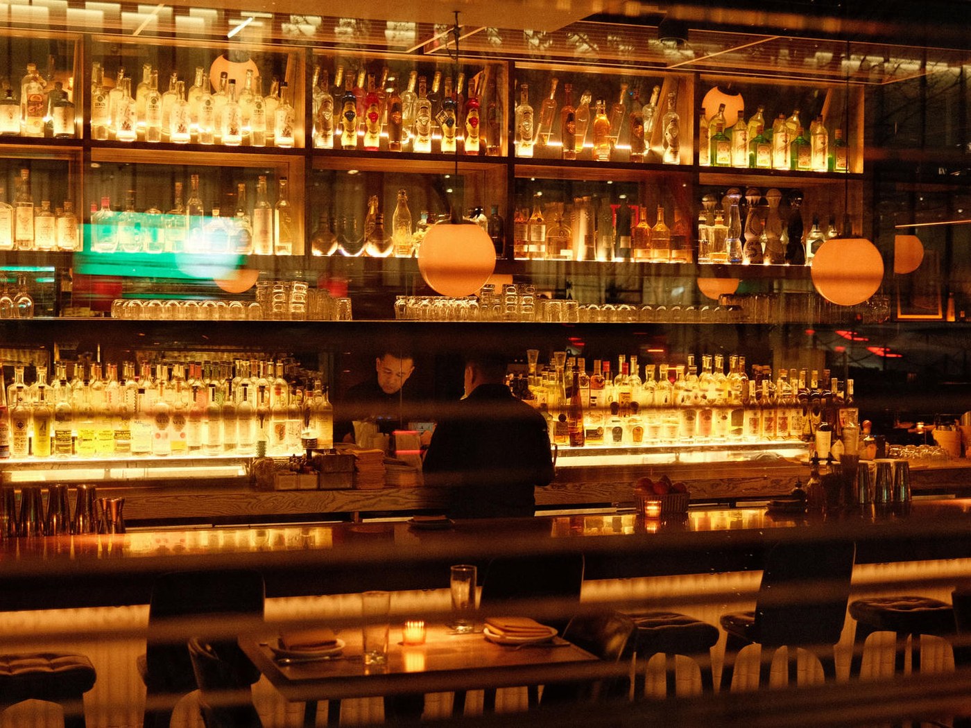 A warm, lit bar with bottles on the shelves and stools at the counter